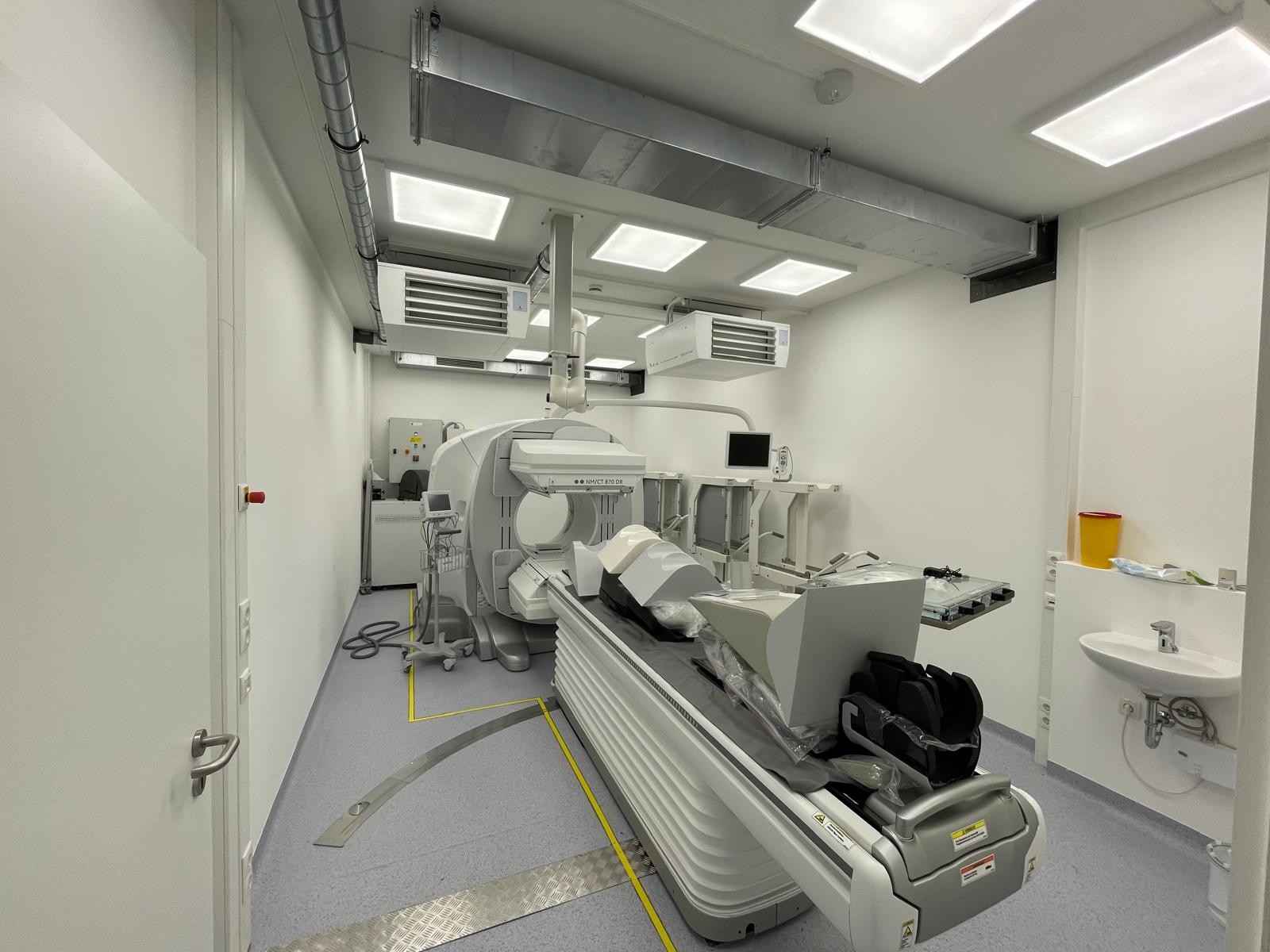 Fertig ausgebauter Untersuchungsraum der temporären SPECT-CT-Einheit mit installiertem Nuklearmedizin-CT, Patientenliege, Deckenlüftung und Handwaschplatz