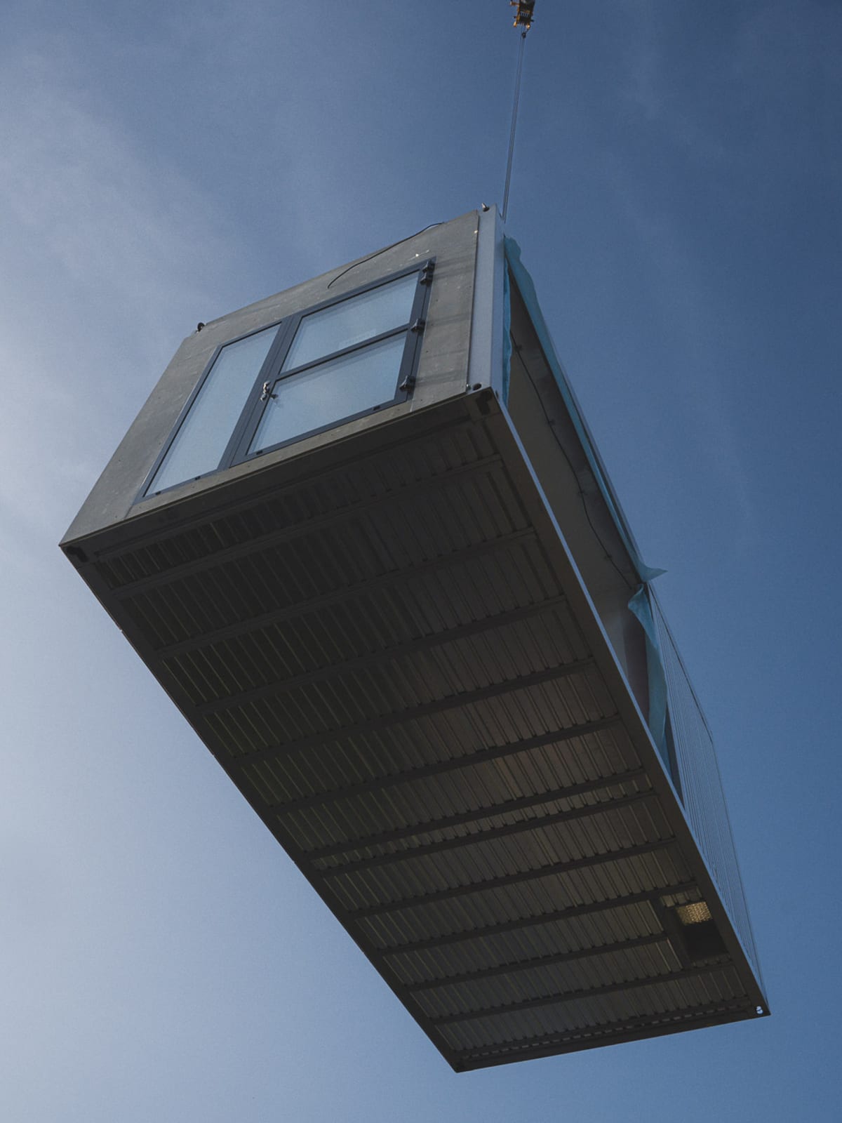 Raummodul am Kranhaken während der Montage vor blauem Himmel